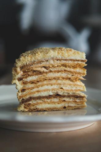 Close-up of a delicate layered cake with smooth cream and gold leaf accents on a minimalist white plate.