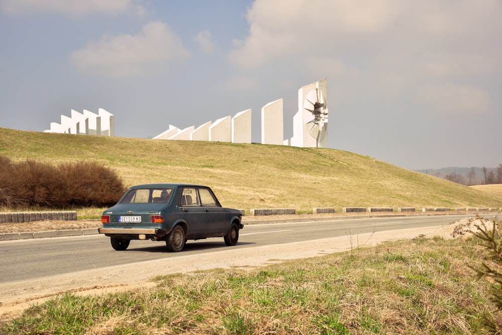 a blue car driving down a road next to a hill