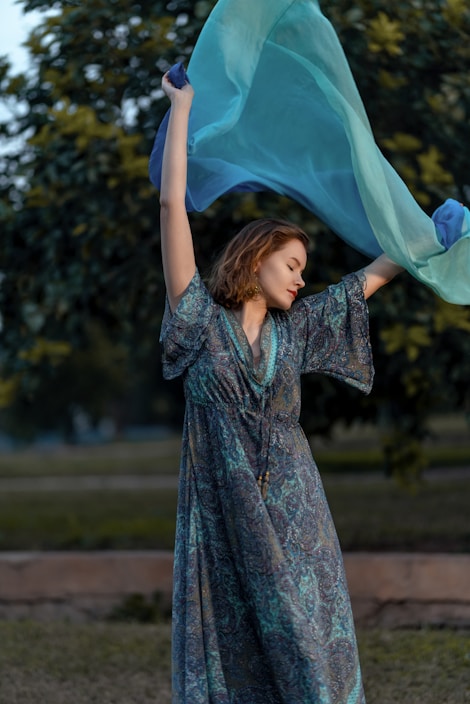 A stylish woman wearing a flowing dress in a vibrant outdoor setting.