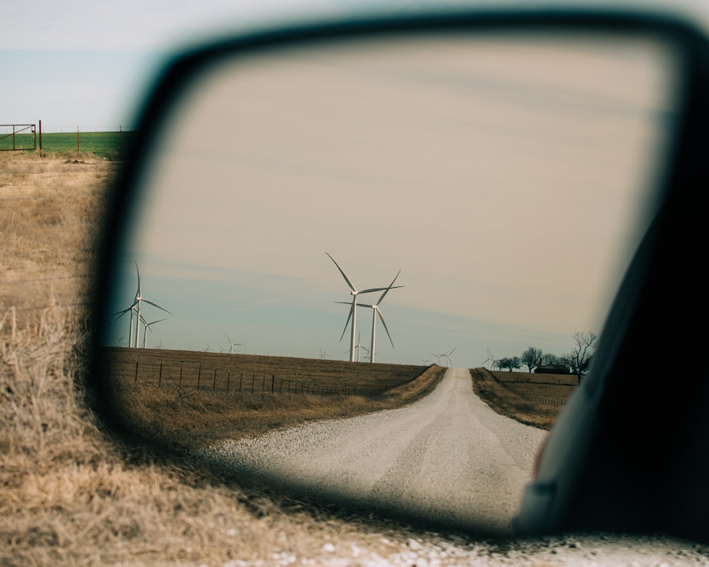 a car's rear view mirror reflecting a wind farm