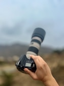 Sleek modern DSLR camera with a zoom lens against a blurred outdoor background.