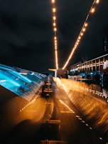 Night view of a completed tensile roof glowing with warm lights over a public space.