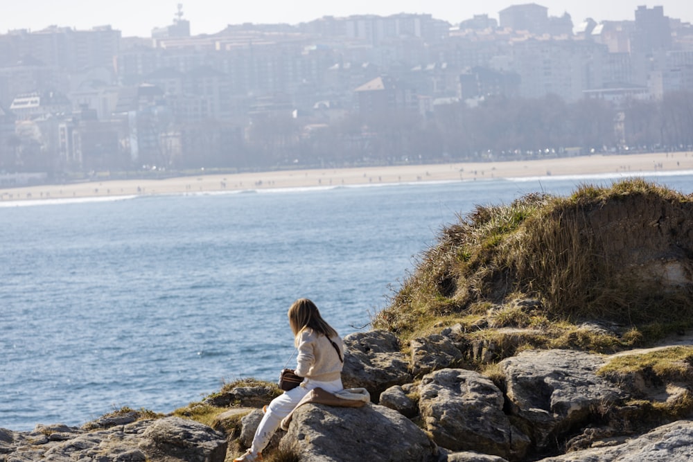 a woman sitting on a rock near the ocean