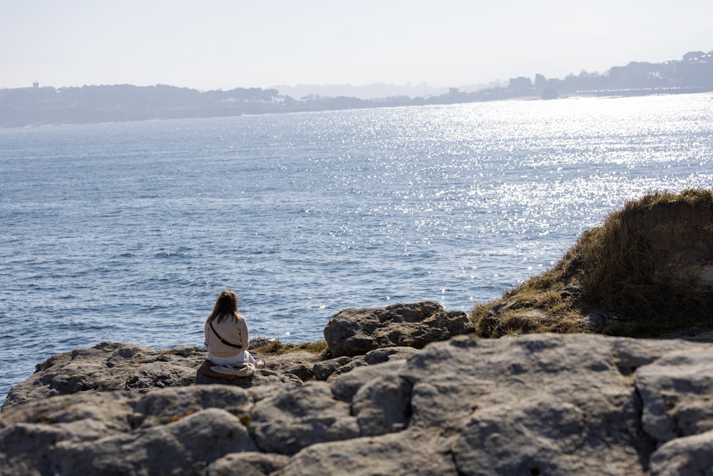 a woman sitting on a rock near the ocean