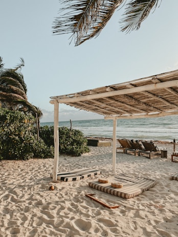 A peaceful meditation spot on the beach with turquoise cushions and flowing white curtains.
