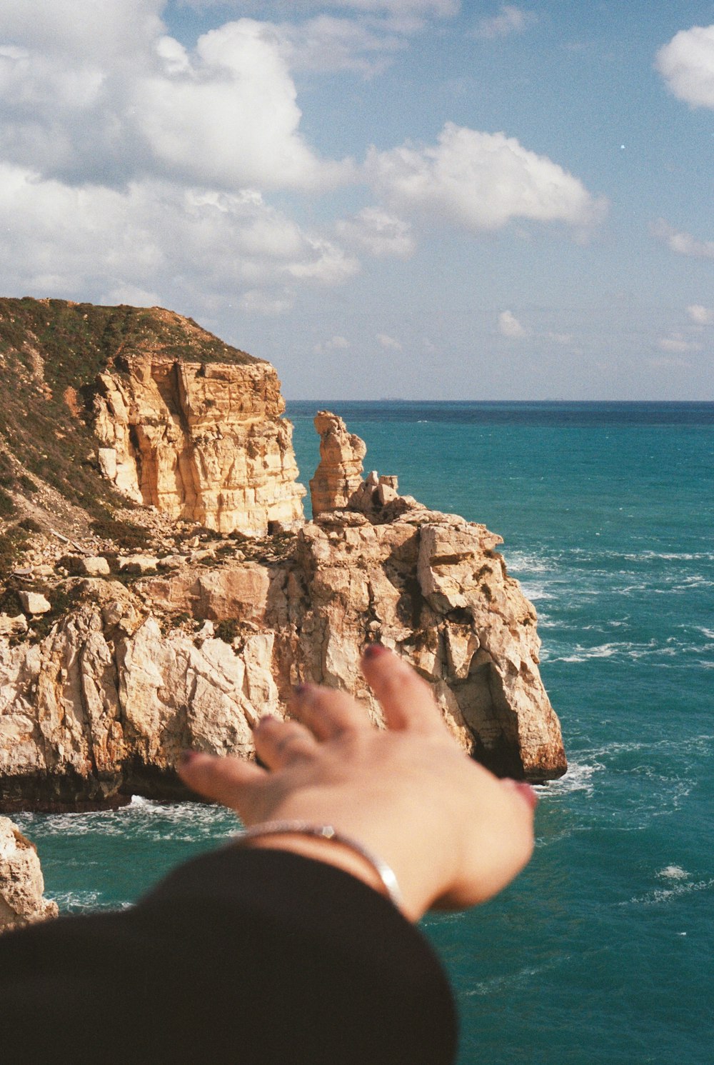 a person reaching out to the ocean from a cliff