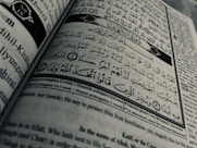 Arabic calligraphy and English text are printed on an open book page, with intricate design elements and a clear division between Arabic verse and its English translation.