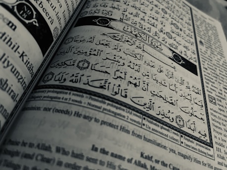 Arabic calligraphy and English text are printed on an open book page, with intricate design elements and a clear division between Arabic verse and its English translation.