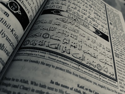 Arabic calligraphy and English text are printed on an open book page, with intricate design elements and a clear division between Arabic verse and its English translation.