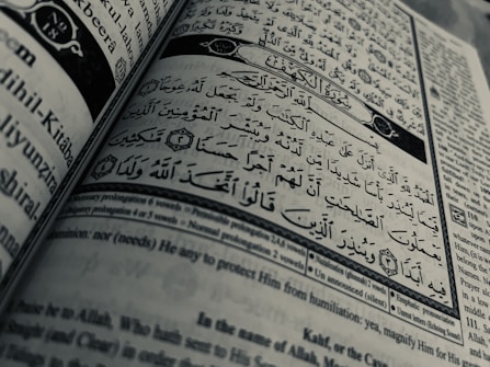 Arabic calligraphy and English text are printed on an open book page, with intricate design elements and a clear division between Arabic verse and its English translation.