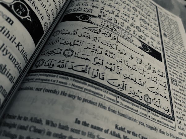 Arabic calligraphy and English text are printed on an open book page, with intricate design elements and a clear division between Arabic verse and its English translation.