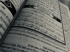 Arabic calligraphy and English text are printed on an open book page, with intricate design elements and a clear division between Arabic verse and its English translation.