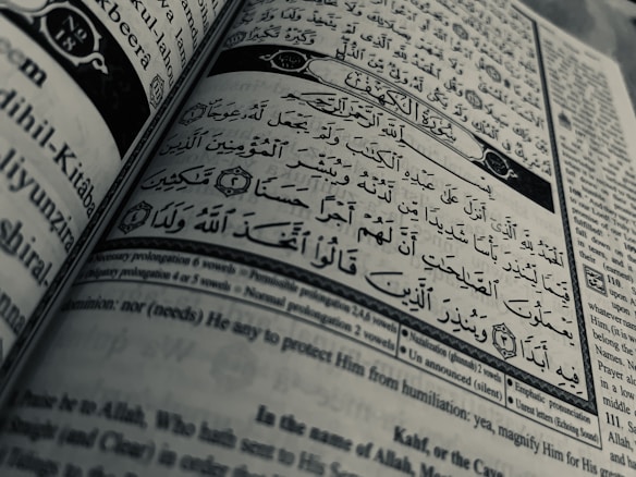 Arabic calligraphy and English text are printed on an open book page, with intricate design elements and a clear division between Arabic verse and its English translation.