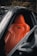 A sleek orange leather car seat is prominently featured inside a luxury vehicle. The design is ergonomic with visible stitching and contouring for comfort. The surrounding area is composed of a dark interior and part of the car's door frame.
