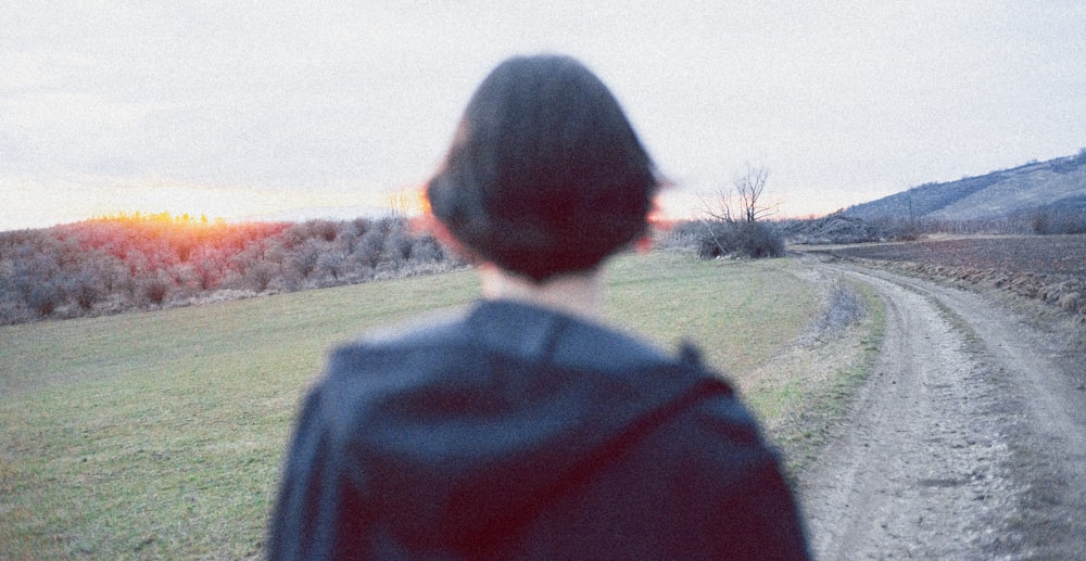 a person standing on a dirt road near a field