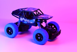 A toy off-road vehicle with blue tires and black body is set against a vibrant pink and purple background. The vehicle's frame is detailed with a pattern and the words 'Super Off-Road' on the side, adding to its rugged appearance.