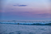 Surfers preparing their boards on a quiet sandy shore at dawn.
