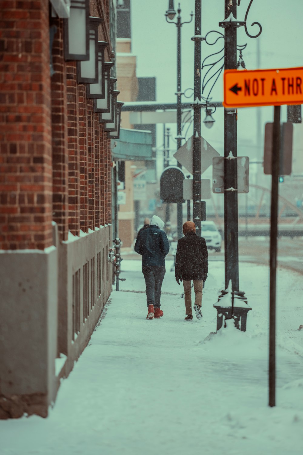 a couple of people walking down a snow covered sidewalk