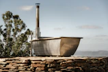 Hot wooden barrel bath steaming gently under open sky with pine trees.