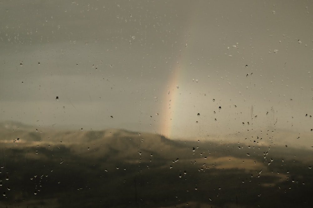 Un arco iris visto a través de una ventana empapada de lluvia