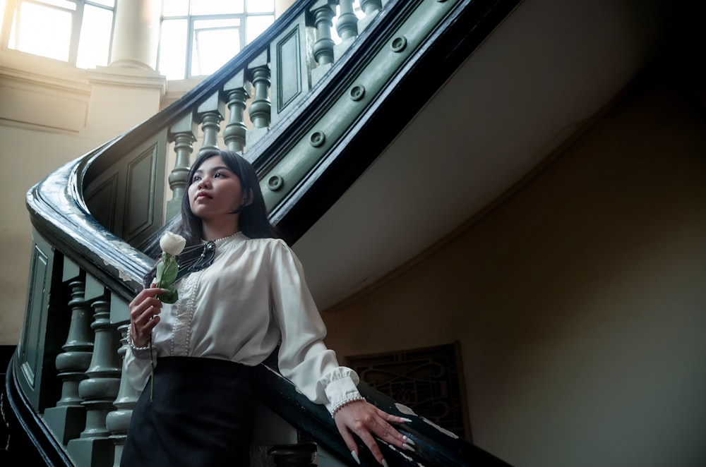 a woman in a white shirt and black skirt standing on a stair case