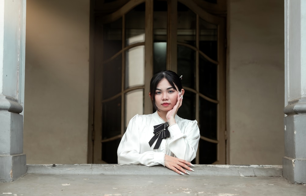 a woman in a white blouse leaning on a window sill
