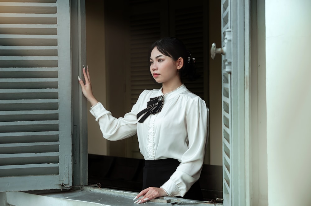 a woman in a white blouse is looking out a window
