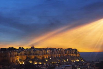 A vibrant sunset over Hanumant Fort, casting warm golden hues on ancient stone walls surrounded by lush greenery.