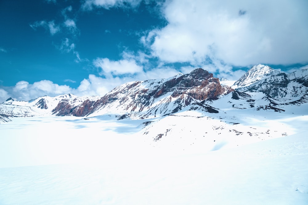 a snow covered mountain range under a cloudy blue sky