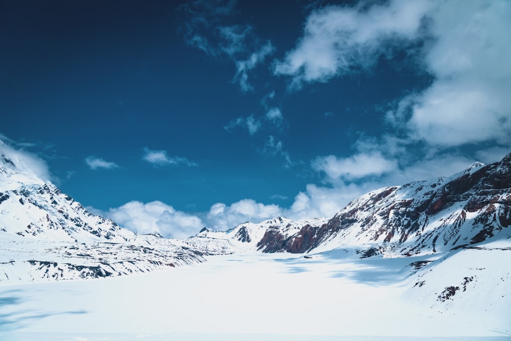 a snow covered mountain range under a cloudy blue sky