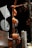 A utility pole is wrapped with several coils of thick orange cables. The cables are organized and bundled around the pole with gray clips. There are attached signs and a traffic light visible, suggesting it's an urban setup. The background is a dark night sky with some leafless tree branches partially visible.