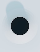 A minimalist abstract design featuring a black circle in the center surrounded by concentric circles that gradually fade into lighter shades of gray and blue. The composition has a clean and symmetrical appearance.