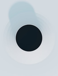 A minimalist abstract design featuring a black circle in the center surrounded by concentric circles that gradually fade into lighter shades of gray and blue. The composition has a clean and symmetrical appearance.