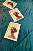 Three framed artworks placed on a dark green quilted surface. The artwork features stylized portraits with a detective theme, including illustrations of figures wearing hats and glasses, with one frame titled 'DETECTIVE'. The frames are positioned diagonally across the surface.