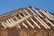 A detailed view of a wooden structure framework under construction, showcasing intersecting beams and trusses with a clear blue sky in the background.