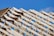 Wooden roof trusses arranged in a triangular pattern against a clear blue sky. Metal connectors hold the beams together, indicating the early stage of construction.
