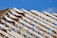Wooden roof trusses arranged in a triangular pattern against a clear blue sky. Metal connectors hold the beams together, indicating the early stage of construction.
