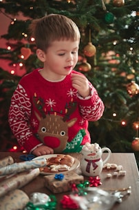 a young boy in a christmas sweater eating cookies