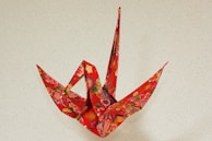 A brightly colored origami crane with intricate floral patterns on a textured light beige background.