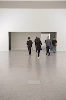 Minimalist gallery room bathed in soft cloud-colored light with visitors engaged in quiet conversation.