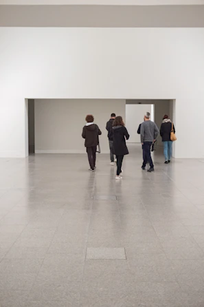 Minimalist gallery room bathed in soft cloud-colored light with visitors engaged in quiet conversation.