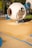 A modern playground structure features a futuristic, spherical design in a neutral, white color. The structure includes circular openings and is connected to a cylindrical tunnel made of blue netting material. The playground area has a soft, rubberized surface with decorative blue lines.