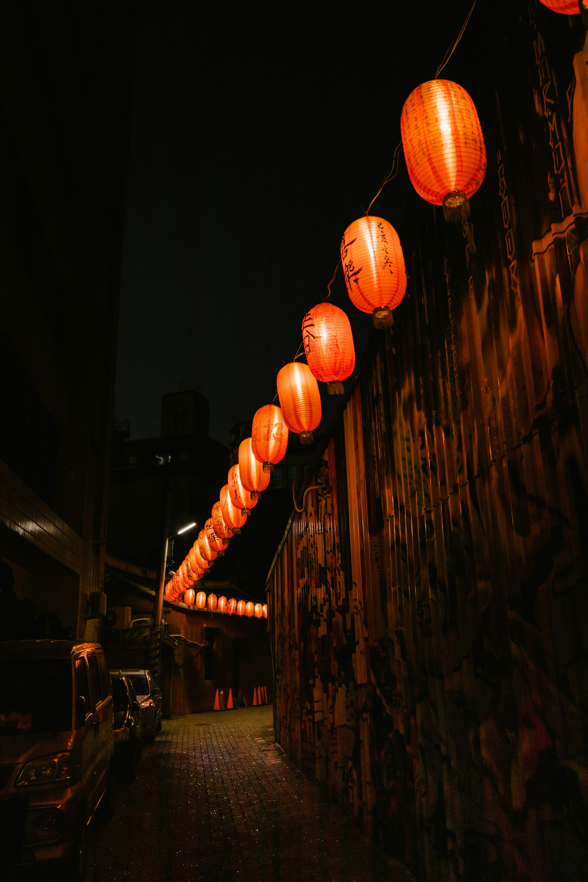 Flickering lanterns lighting a narrow, fog-filled alleyway where ghostly whispers seem to linger in the cold night air.