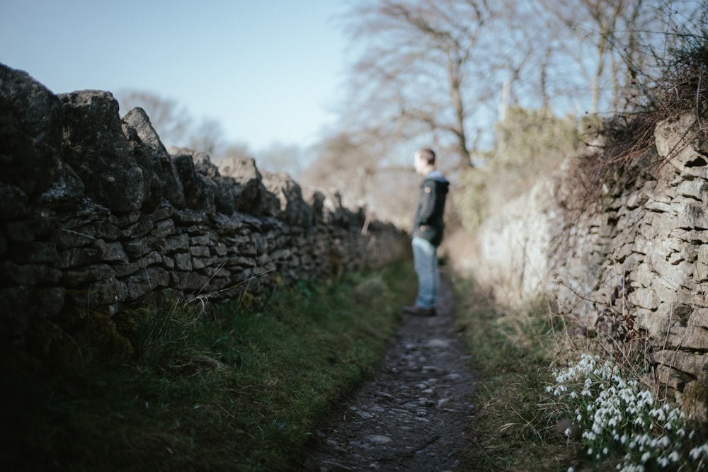 a person standing on a path next to a stone wall