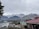 A scenic view of snow-capped mountains in the background with a clear sky. In the foreground, there are several buildings with red and green roofs, surrounded by trees and a well-maintained garden. The landscape is calm and picturesque.
