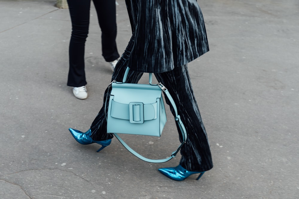 a woman carrying a light blue bag while walking down the street