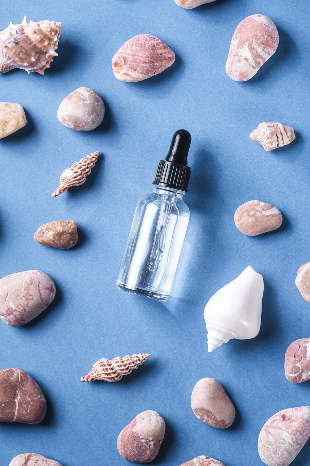Dropper bottle on blue with shells and pebbles