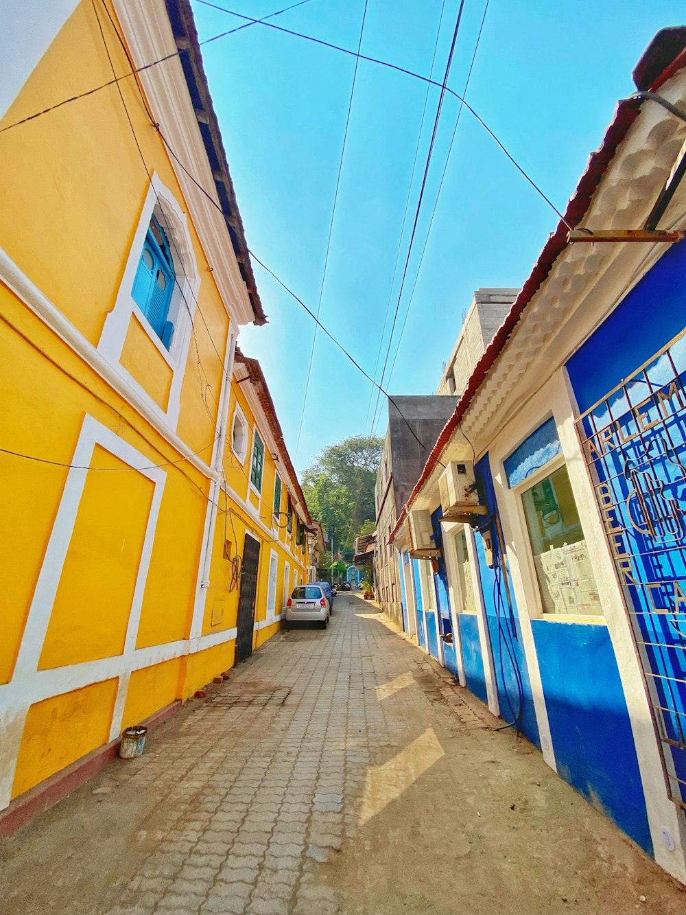 a narrow street with a yellow building and blue windows