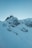 A snowy mountainside with a building at the top, featuring an observatory or antenna structure with a dome and radar equipment. The landscape is rugged with exposed rock formations covered in snow, creating a serene and isolated atmosphere.