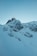 A snowy mountainside with a building at the top, featuring an observatory or antenna structure with a dome and radar equipment. The landscape is rugged with exposed rock formations covered in snow, creating a serene and isolated atmosphere.